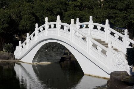 Chinese style bridge going over a lake, in a public space. This bridge is white.の写真素材