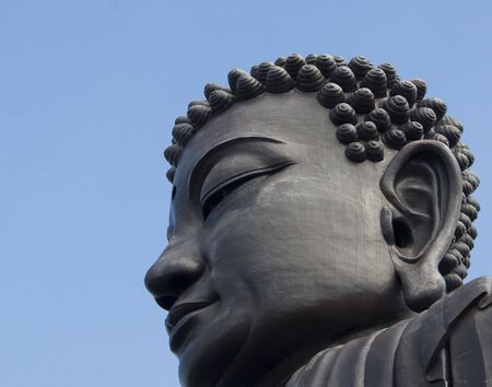 This is the head of a large buddha against a blue sky backdrop.  の写真素材