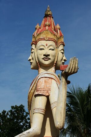 A Thai style Buddhist sculpture with four heads against a blue sky background.  This was at a Thai Buddhist temple. の写真素材