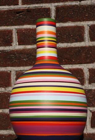 A multi-coloured vase is set against a brick wall.   The vase is full of color, including green, red, purple, yellow, white, blue, orange and pink. の写真素材