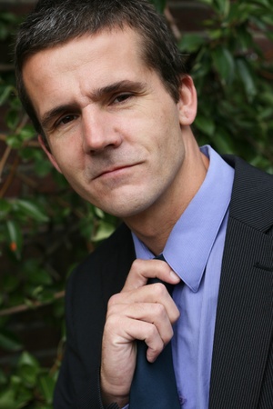 A man dressed in a suit has a hand on his tie. He looks like heの写真素材