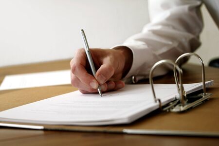 Someone is writing on a document in an official looking folder の写真素材