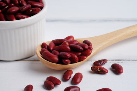 Dried red beans in cup and spoon on white wood table background, selective focus, close up.