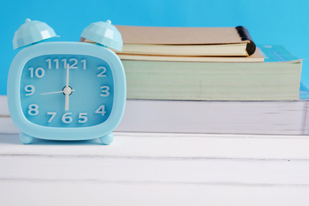 Blue alarm clock and decorated book on white wood and blue background concept.