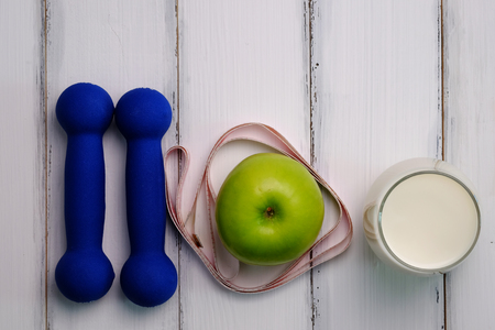 The concept of weight loss with dumbbell, apple, milk and measuring on white wood background style. Top view.の写真素材