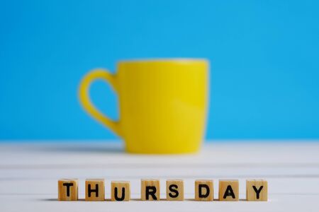 Close up of Thursday in letter wooden block selective focus on white wood table and blue background concept. Yellow cup decoration style.の写真素材