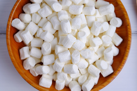Top view of small size white marshmallows isolated in wood cup on background.
