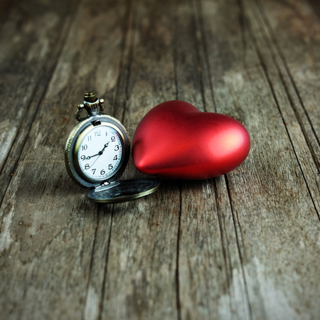 Close up of Red heart and classic clock on wood background, vignette effect concept. Time concept and love, vintage style and selective focus.の写真素材