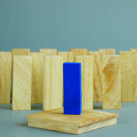 Blue one wooden block standing from other standing in row on gray background. Business concept metaphor to leadership for survive. Selective focus dominant wooden block.の写真素材
