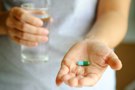 Close up with pill and glass of water on hand, medicine concept, selective focus.の写真素材