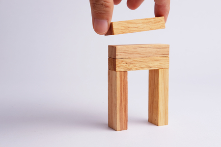 Business man hand pick and put of wooden block tower in shape on gray background. Selective focus and blank space. Business concept for process teamwork and growth success process.の写真素材