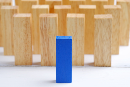 Blue one wooden block standing from other standing in row on white wood background. Business concept metaphor to leadership for survive. Selective focus dominant wooden block.の写真素材