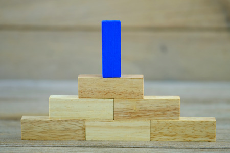 Blue one wood block on wood block step stair of pyramid on wood background. Business concept for growth success process. Selective focus on the top step.の写真素材