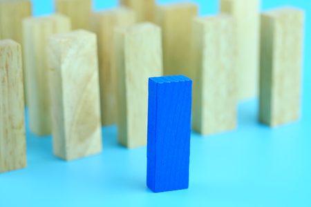 Blue one wooden block standing from other standing in row on blue background. Business concept metaphor to leadership for survive. Selective focus dominant wooden block.の写真素材