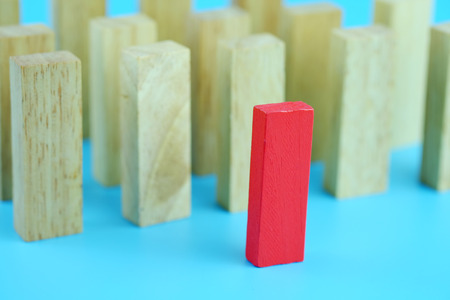 Red one wooden block standing from other standing in row on blue background. Business concept...