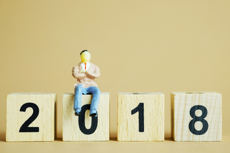 Close up of Happy new year with Businessman miniature figure toy sit on stack of number 2018, on brown background and selective focus.の写真素材