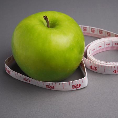 Green apple with measure tape and diet symbol concept on gray background, close up, selective focus.の写真素材