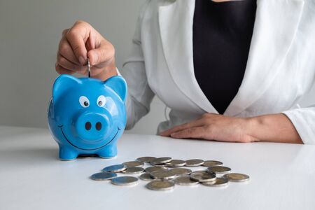 women hand putting coin into blue piggy bank saving money with coins pile.の写真素材