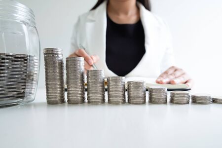 woman hand writing coins in glass bottle bank with coins bar graph, step up growing business to success and saving for retirement concept.の写真素材