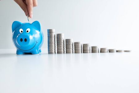 hand putting coin in blue piggy bank with coins bar graph, step up growing business to success and saving for retirement concept.の写真素材