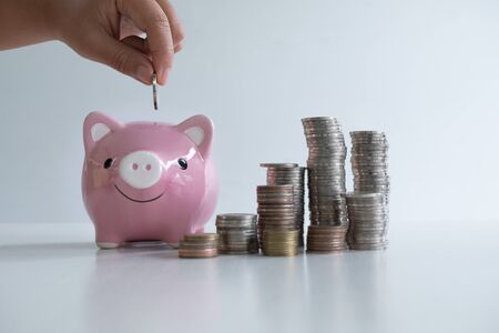 hand putting coin in pink piggy bank with coins pile, step up growing business to success and saving for retirement concept.の写真素材