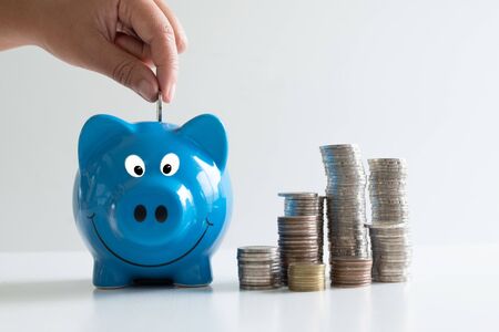 hand putting coin in blue piggy with coins pile, step up growing business to success and saving for retirement concept.の写真素材