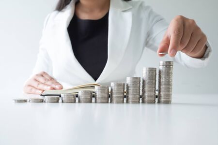 one woman putting coin on growth coins graph in white suit,step up growing business to success and saving for retirement concept.の写真素材