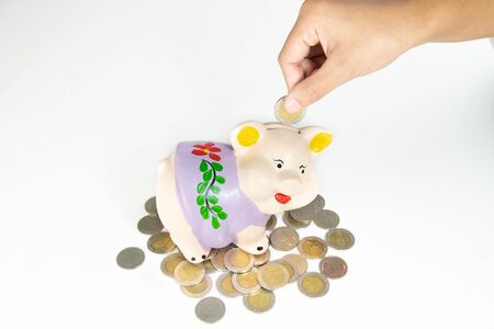 hand putting coin into Purple piggy bank saving money with coins pile.の写真素材
