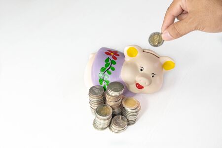 hand putting coin into Purple piggy bank with coins pile.の写真素材
