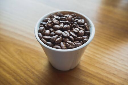 Coffee bean in white ceramic cup with brown wooden background.の写真素材