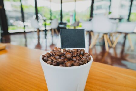 Coffee bean in white ceramic cup and black flag with brown wooden background.の写真素材
