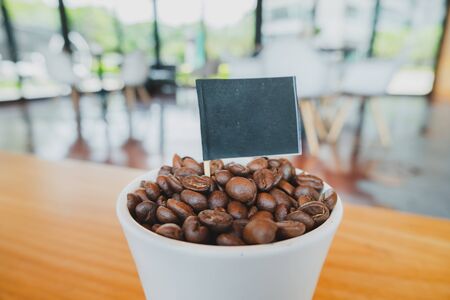 Coffee bean in white ceramic cup and black flag with brown wooden background.の写真素材