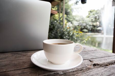 A cup of coffee on the wooden table behide laptop.の写真素材