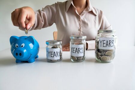 Business woman putting coin into blue piggy bank with 3 years planing account , step up growing business to success and saving for retirement  concept.の写真素材