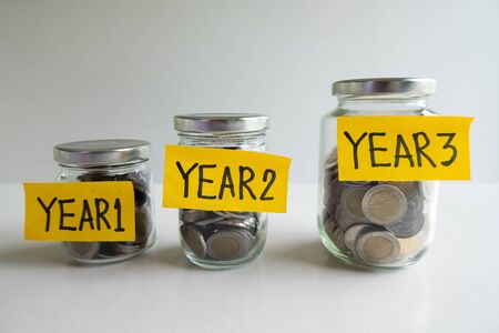 Glass piggy bank with 3 years saving money plan, step up growing business to success and saving for retirement  concept.の写真素材