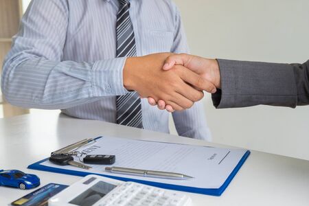 shaking hands, Car dealership provides advice about insurance details and car rental information and delivers the keys after signing the rental contract.の写真素材