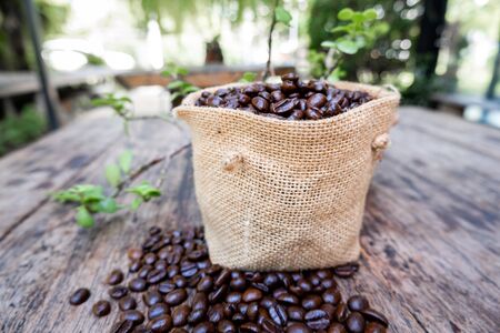full of coffee beans spilling out bag on brown wooden background.の写真素材