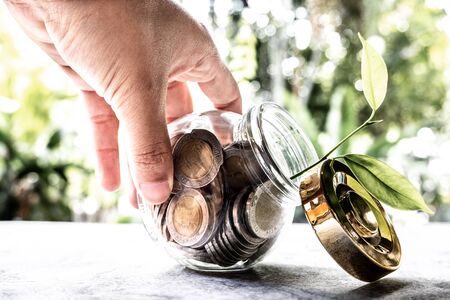 hand and Glass jar piggy bank with coins. Plan your savings, run a growing business for success and save for retirement.の写真素材