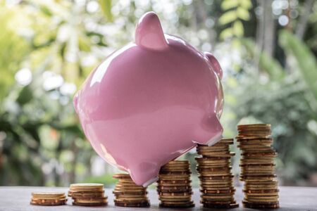Pink piggy bank and golden coins pile on wooden table with the natural background, step up growing business to success and saving for retirement concept.の写真素材