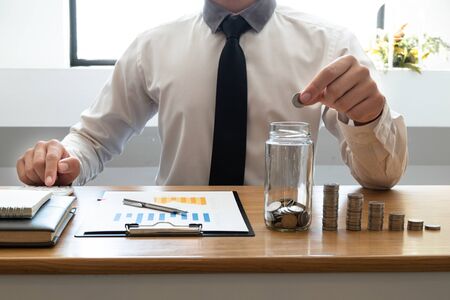 Business men laying coins down In a glass bottle next to the coin chart, expanding a successful and economical business for retirement concepts.の写真素材