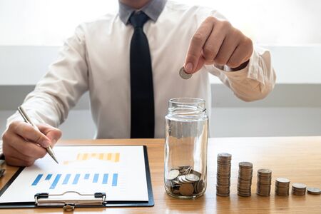 Business men laying coins down In a glass bottle next to the coin chart, expanding a successful and...