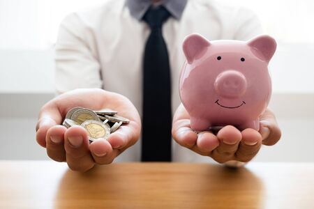 The hands of a businessman who holds a coin with a piggy bank to save money in stepping into a business that has grown up for retirement success.の写真素材