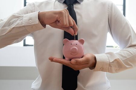 The hand of a businessman who holds a coin with a piggy bank to save money, grow a successful business, and save for retirement concept.の写真素材