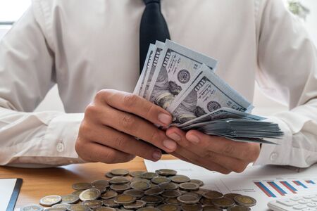 Businessmen holding dollars and coins in front, calculate graphs to save money, expand successful businesses and save for retirement.の写真素材