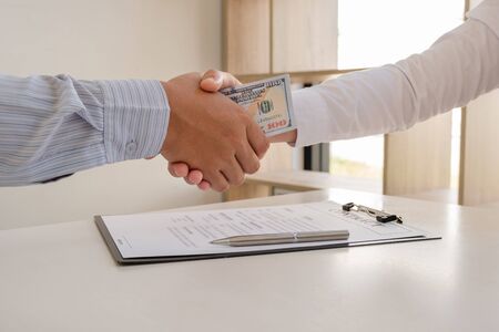 photo of Businessmen shake hands and dollar note, sign a contract to bribe corruption in the company. The concept of bribery and corruption.の写真素材