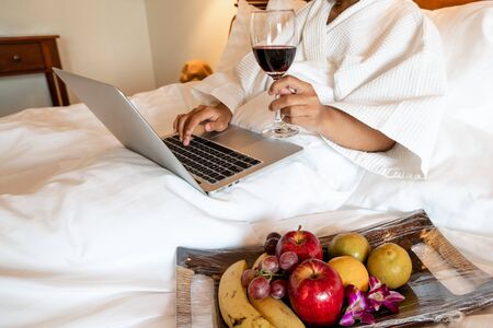 The hand of Young woman that hold wine glass And Sit play laptop In a luxurious room Ready Fruit.の写真素材