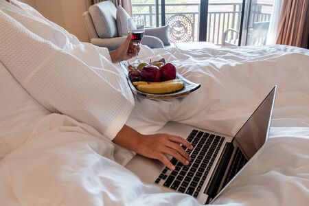 The hand of Young woman that hold wine glass And Sit play laptop In a luxurious room Ready Fruit.の写真素材