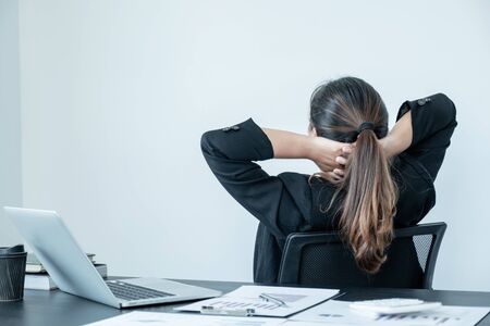 A young woman working in an office with her back to sit and relax on an office chair.の写真素材