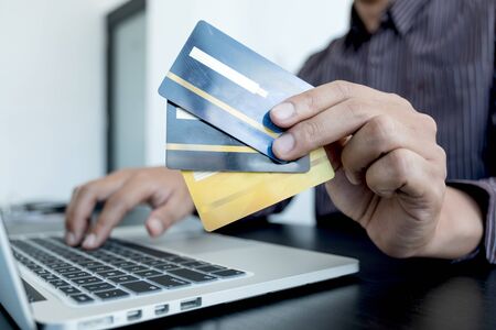 The businessman's hand is holding a credit card and using a laptop for online shopping and internet...