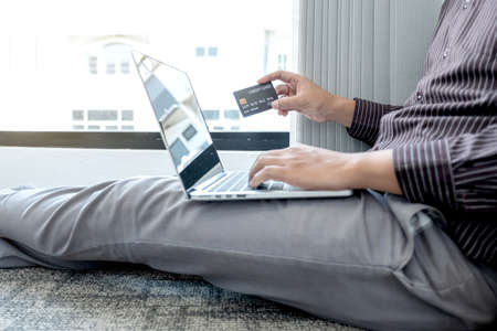 The businessman's hand is holding a credit card and using a laptop for online shopping and internet payment in the office.の写真素材